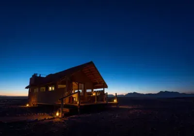 Kulala Desert lodge illuminated at dusk with warm lights in the desert against a twilight sky