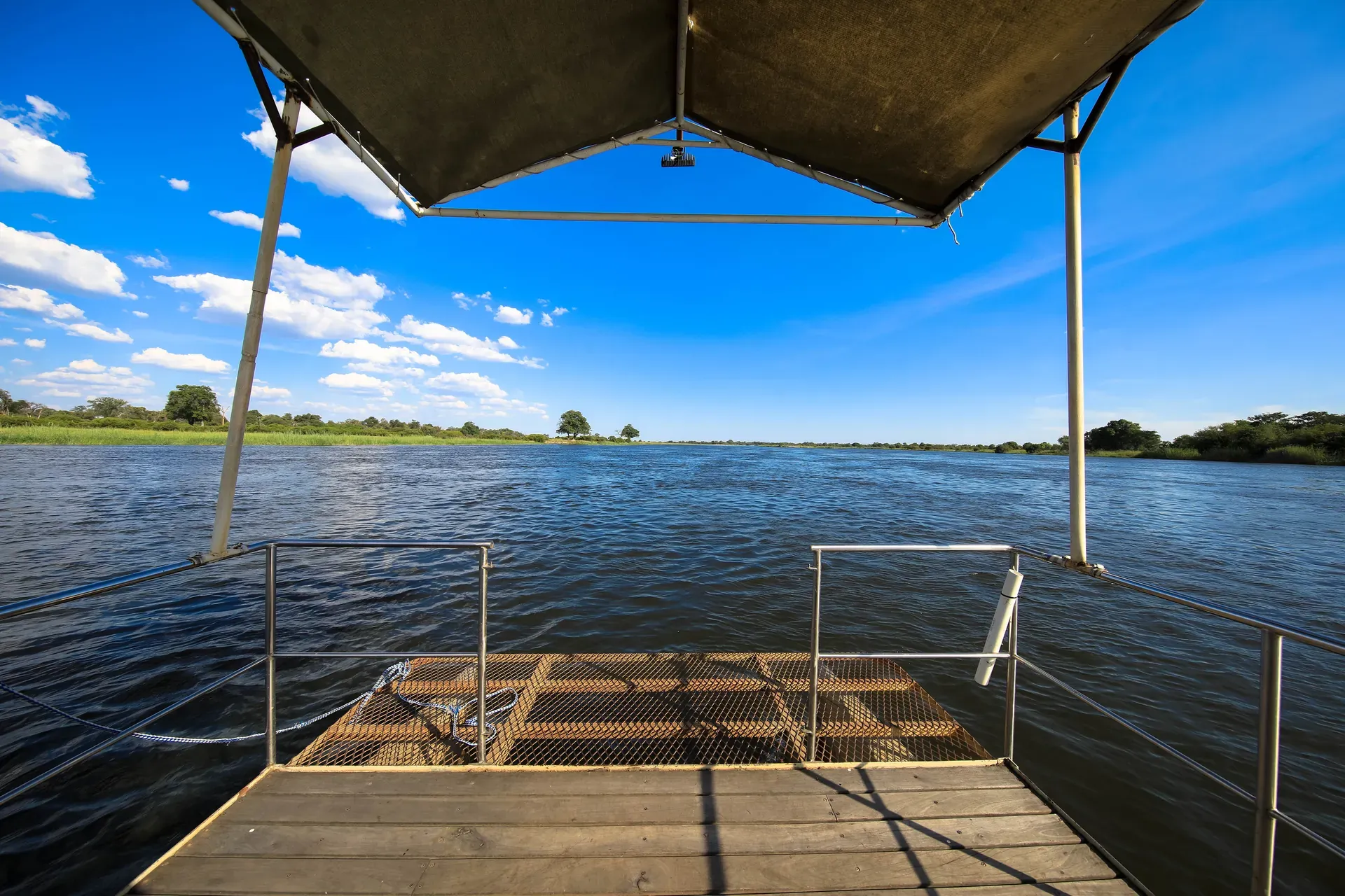 View from a boat cruise under a canopy overlooking calm water and blue skies