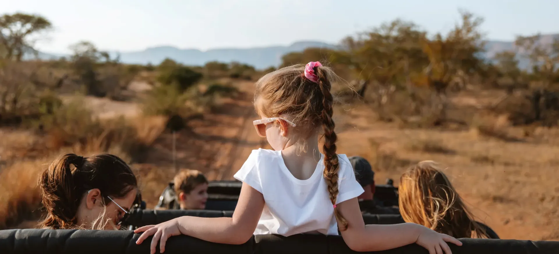 Young girl on safari wearing a hat, sitting in an open-air vehicle and enjoying the adventure