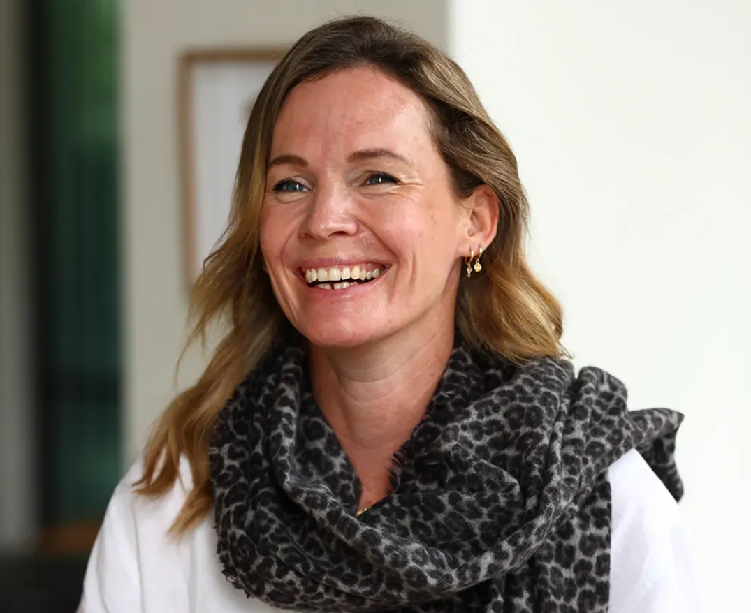Smiling woman with long brown hair wearing a white blouse and patterned scarf