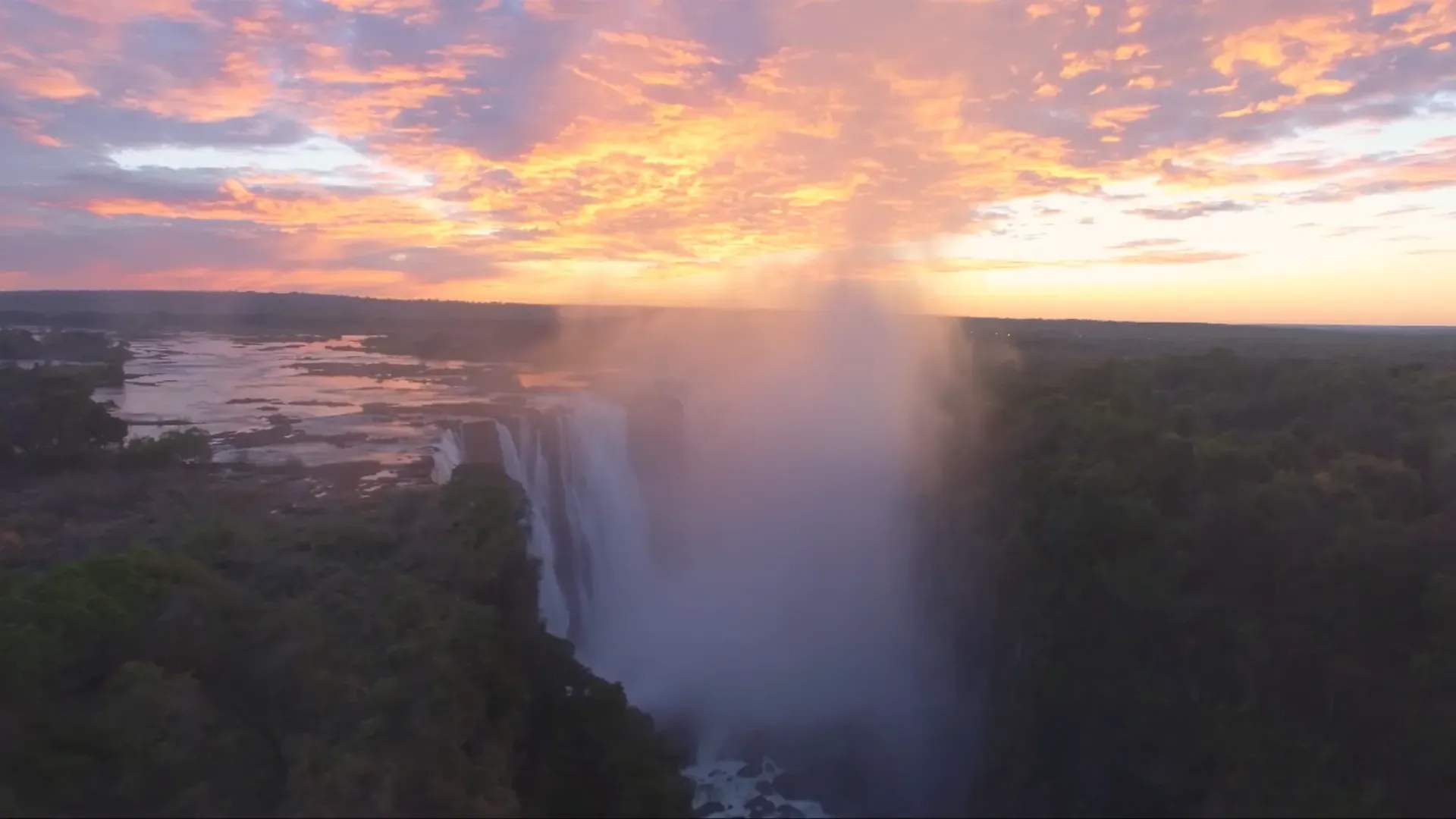 Sunrise view of a powerful waterfall plunging into a misty gorge under pink and blue February skies