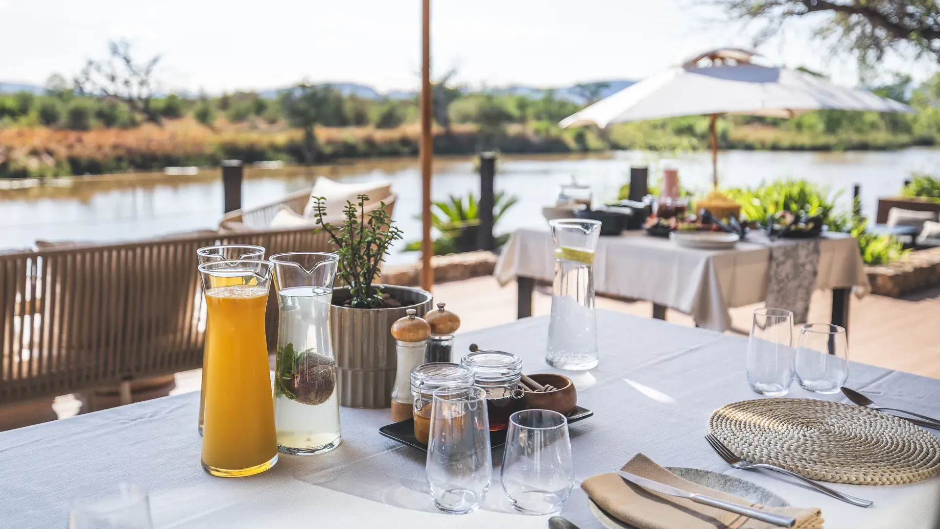 Breakfast table set up on an outdoor deck overlooking the landscape with white tablecloth and chairs