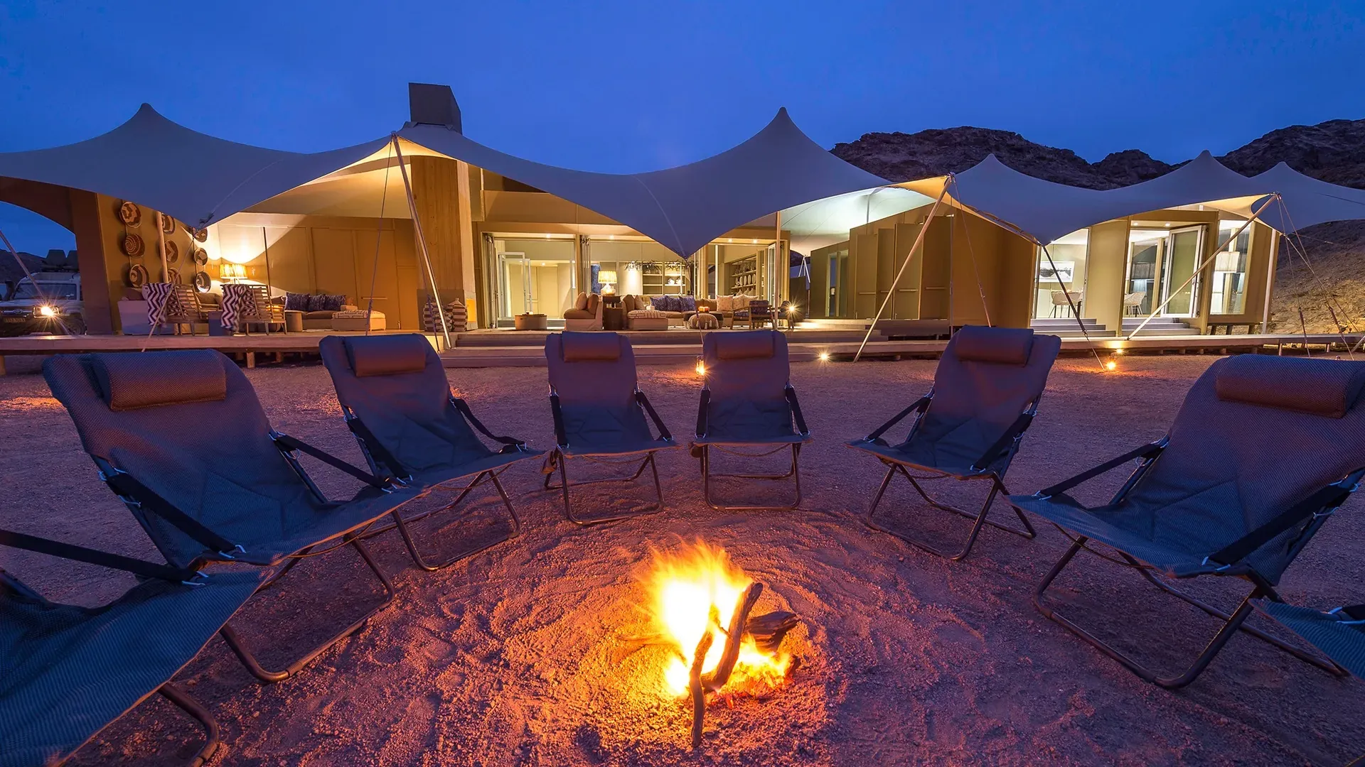 Wilderness Hoanib Skeleton Coast Camp at night with chairs around a glowing campfire and tented suites under a starry desert sky