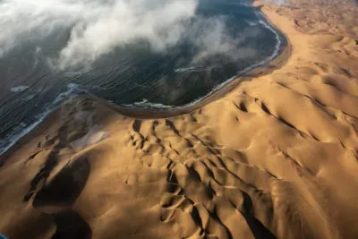 Aerial view of a dramatic coastal encounter where turquoise ocean waves meet golden desert sand