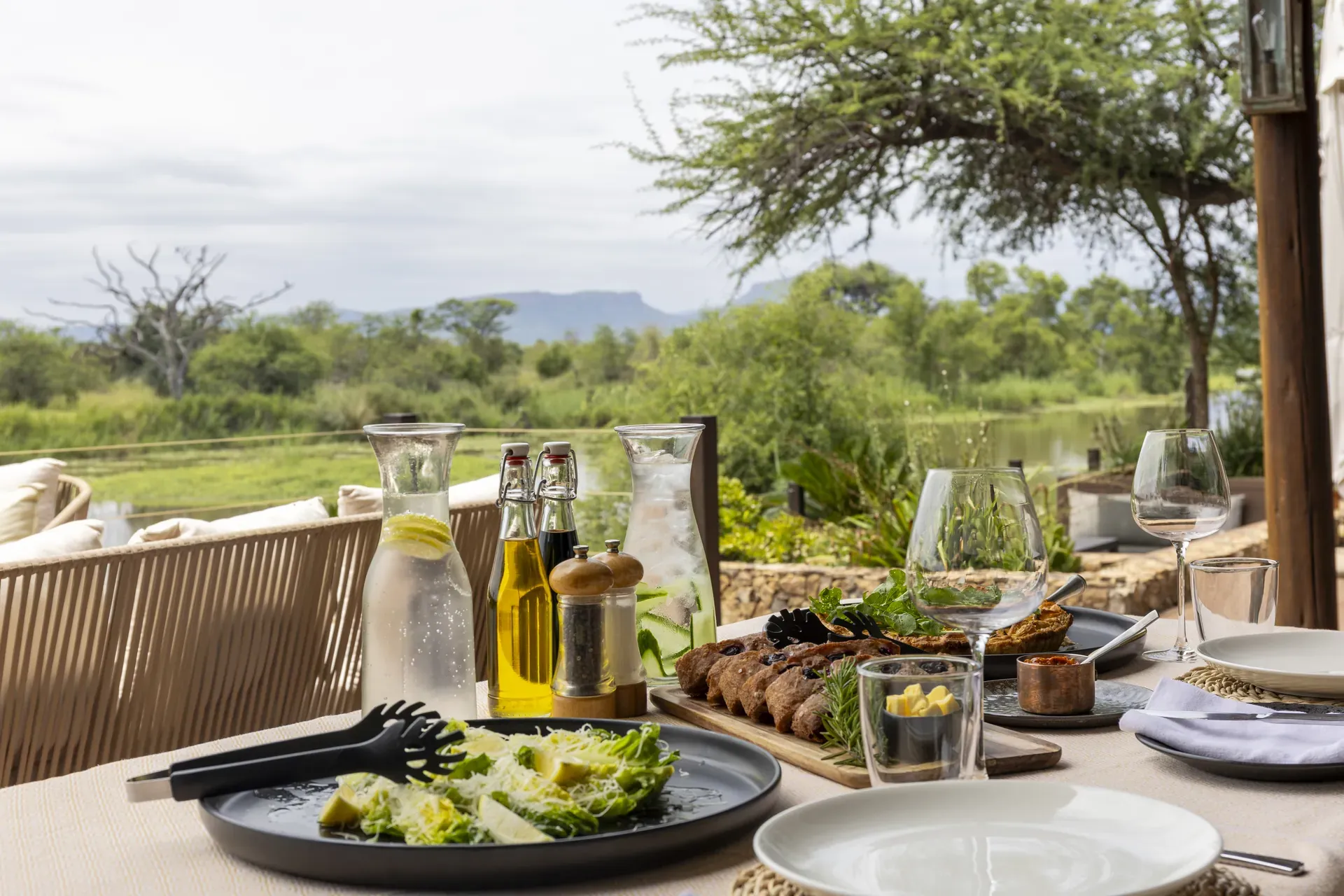 Outdoor group dining setup with a long table and chairs arranged under trees for a communal meal