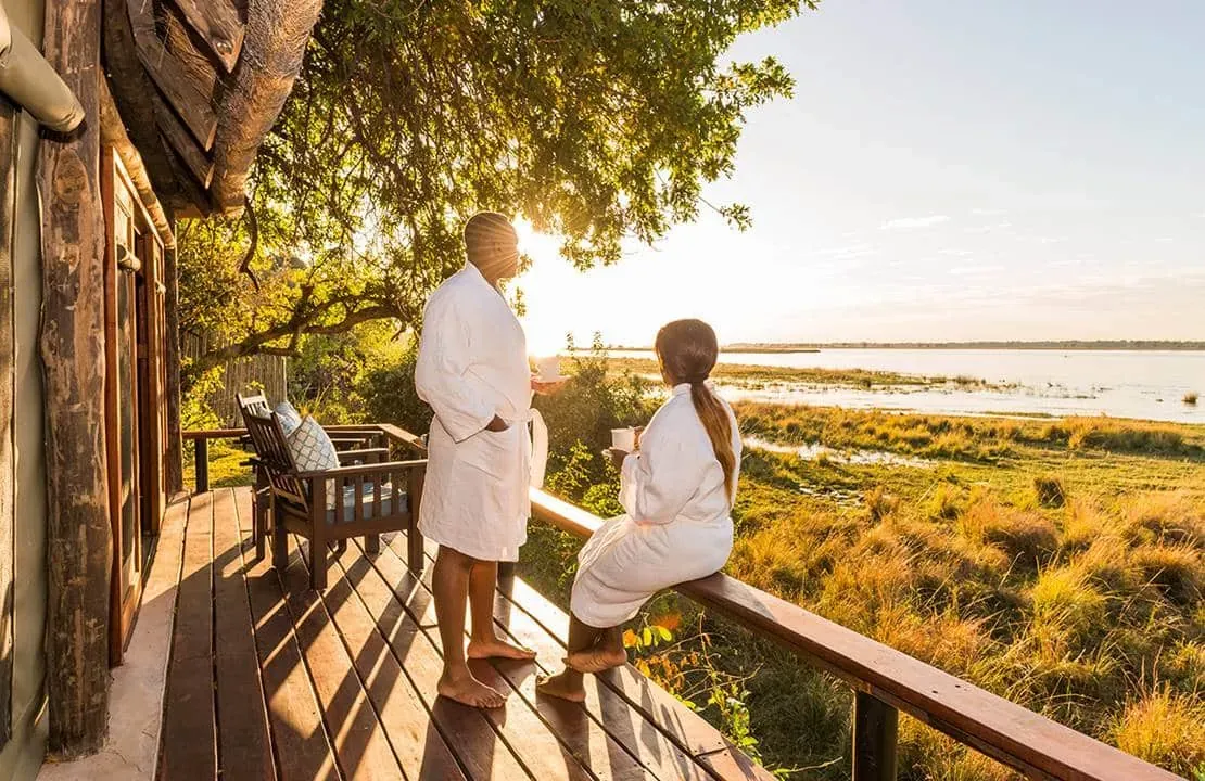 Couple walking hand in hand along a wooden walkway leading to a secluded lodge surrounded by greenery