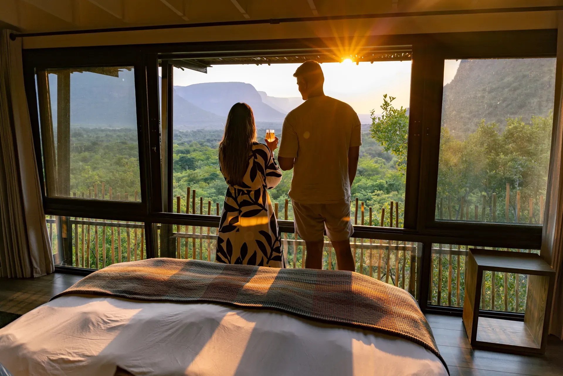 Couple looking out of a window at sunset with scenic bush and mountain views at Marataba.