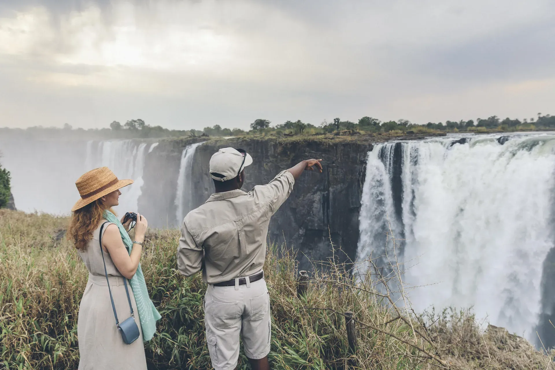 Tourist standing at a scenic viewpoint overlooking Victoria Falls with cascading water and lush cliffs