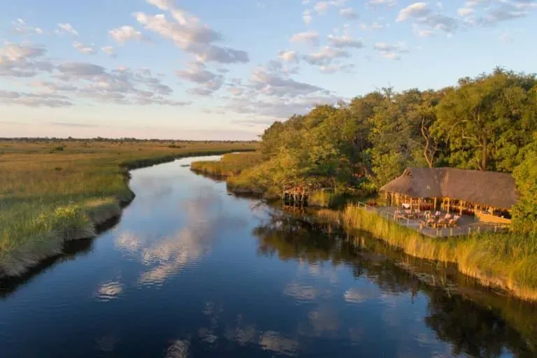 Scenic view at Camp Xakanaxa with calm river reflecting trees and blue sky