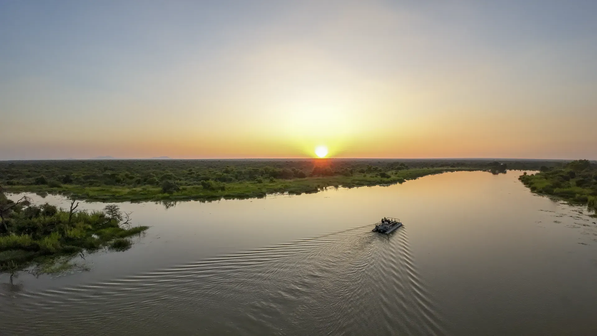 Boat cruising on a calm river at sunrise with reflections of the golden sun on the water