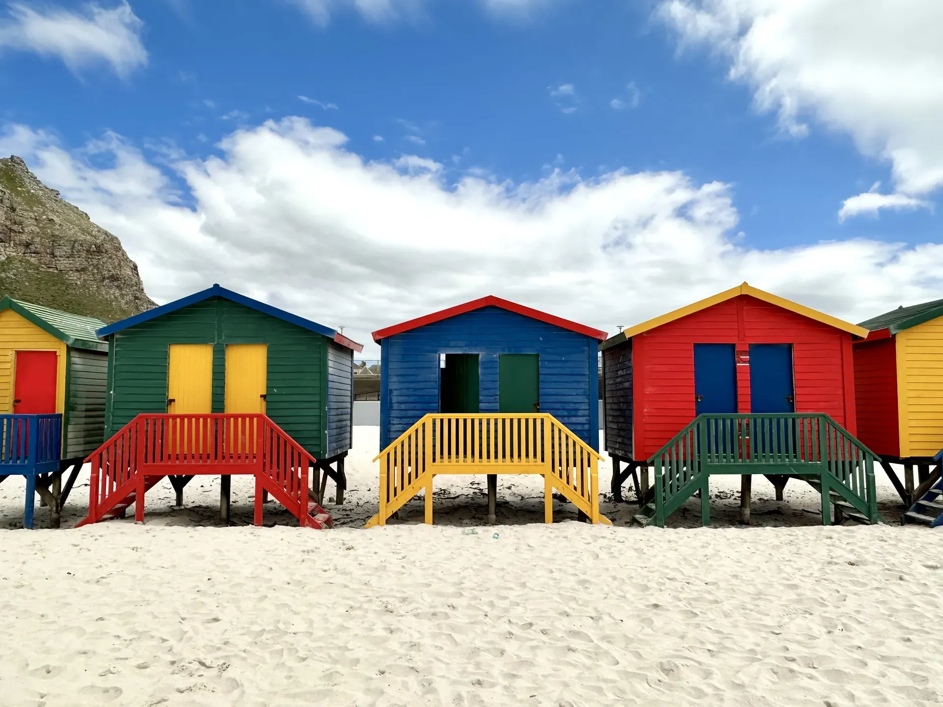 Colorful beach huts in Cape Town near Table Mountain with blue sky and white sandy beach